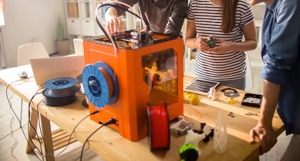 3D yazıcı kullanan insanlar ve turuncu renkli 3D yazıcı örneği.